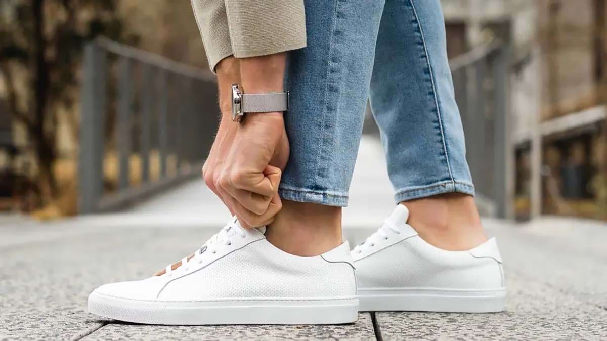 Person in jeans adjusting their GREATS sneakers